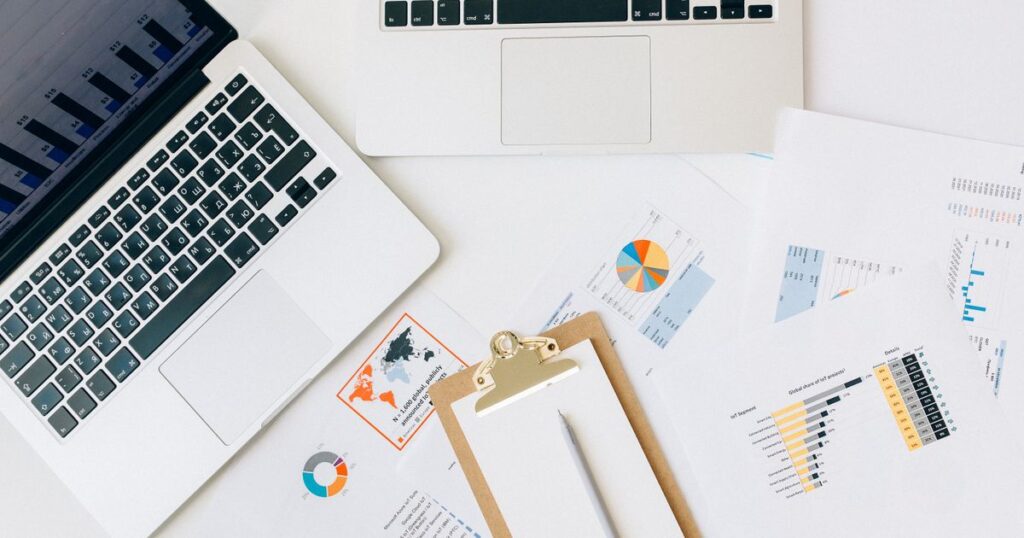 Overhead view of two laptops and printed marketing charts spread across a desk for comparing channel performance.