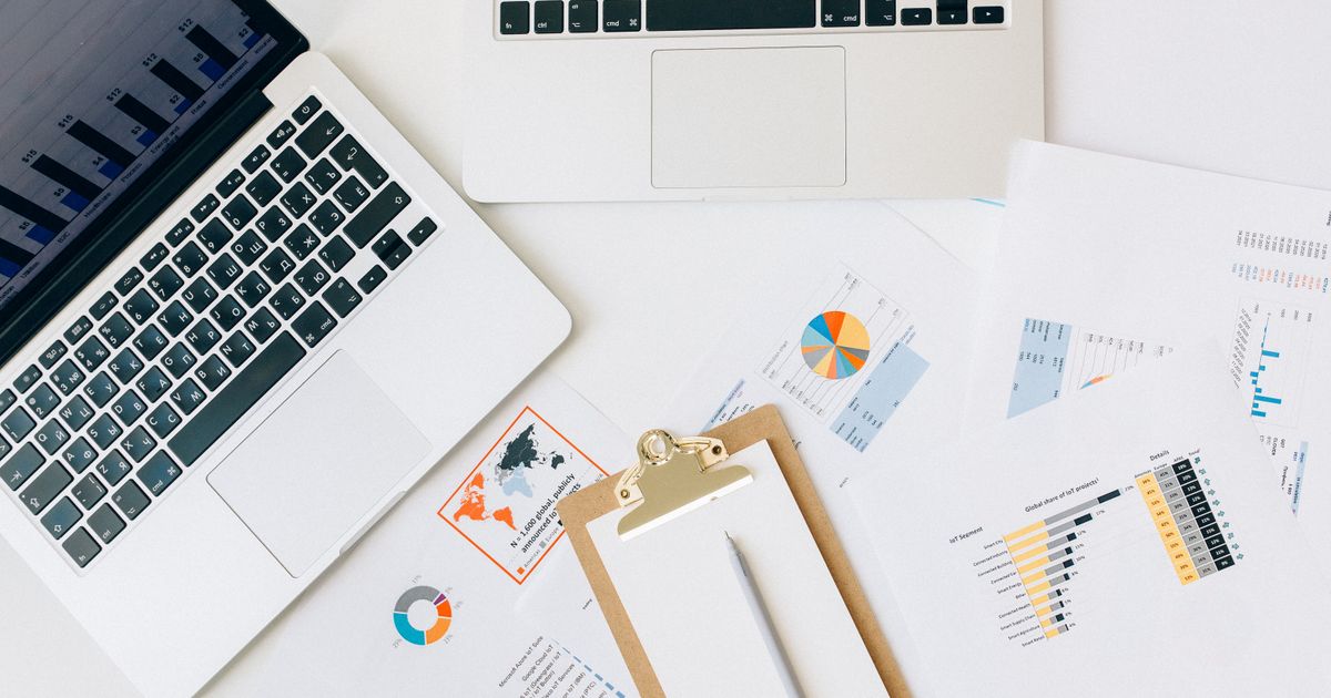 Overhead view of two laptops and printed marketing charts spread across a desk for comparing channel performance.