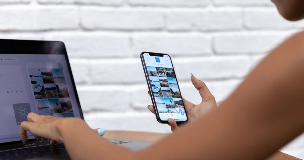 Social media manager replying to customer messages on a smartphone while working at a laptop.