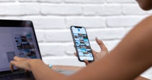 Social media manager replying to customer messages on a smartphone while working at a laptop.