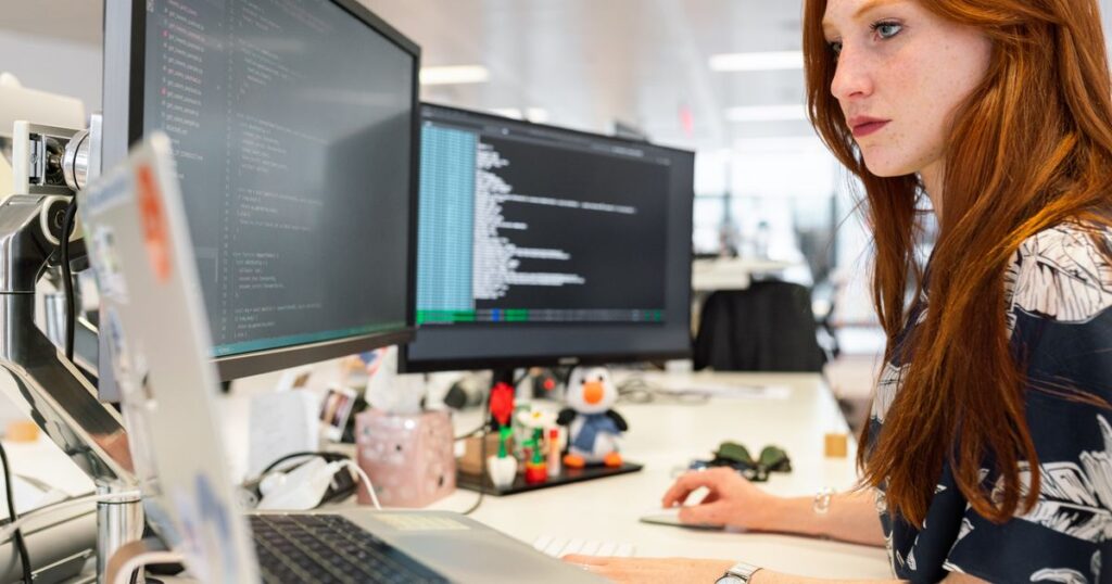 Developer working on website tracking code across dual monitors in an open-plan office.