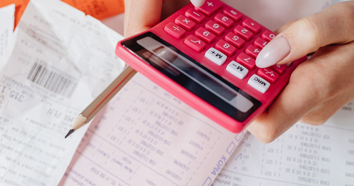 Hands using a calculator surrounded by financial documents, representing Google Ads costs
