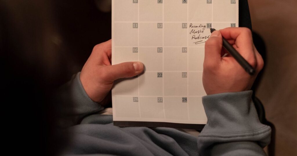Person planning social media content on a paper calendar, illustrating how often to post on social media.