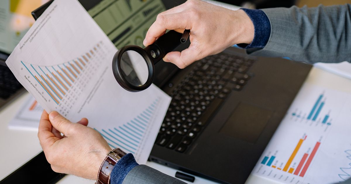 Businessman examining data charts with a magnifying glass over a laptop, representing an SEO audit