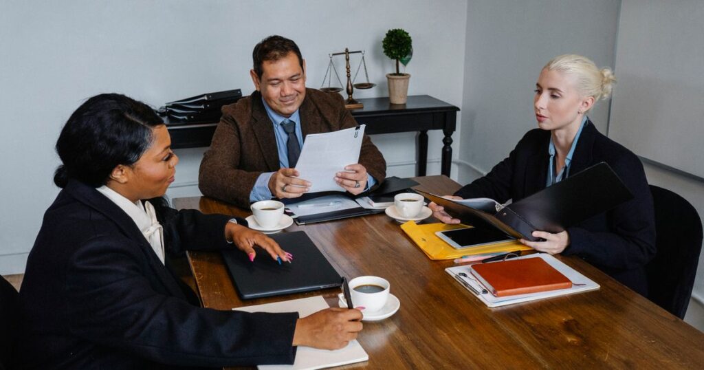 Group of business professionals in formal attire discussing strategy around a meeting table