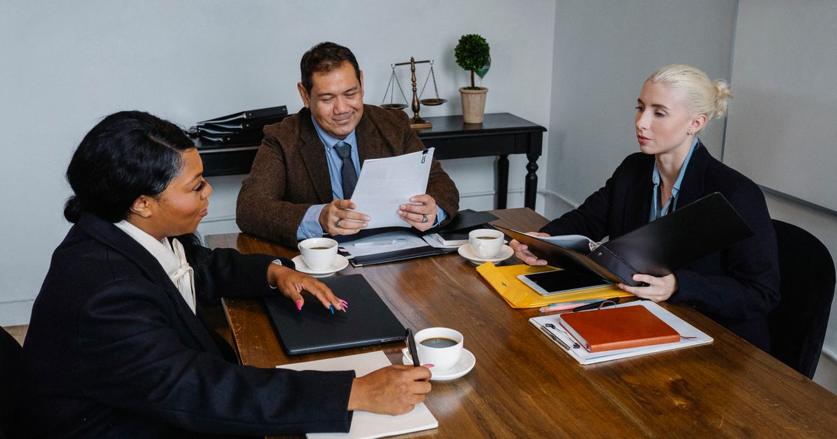Group of business professionals in formal attire discussing strategy around a meeting table