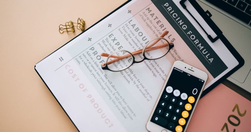 Overhead view of a desk with a calculator, pricing formula documents and eyeglasses, used to work out cost per lead