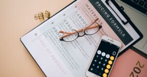 Overhead view of a desk with a calculator, pricing formula documents and eyeglasses, used to work out cost per lead