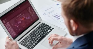 Marketer reviewing a data dashboard on a laptop beside printed performance charts