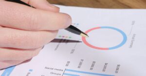 Marketer reviewing printed performance charts with a pen while planning a social media budget split.