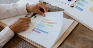 Hands reviewing a printed marketing report with colourful charts and graphs on a wooden desk.