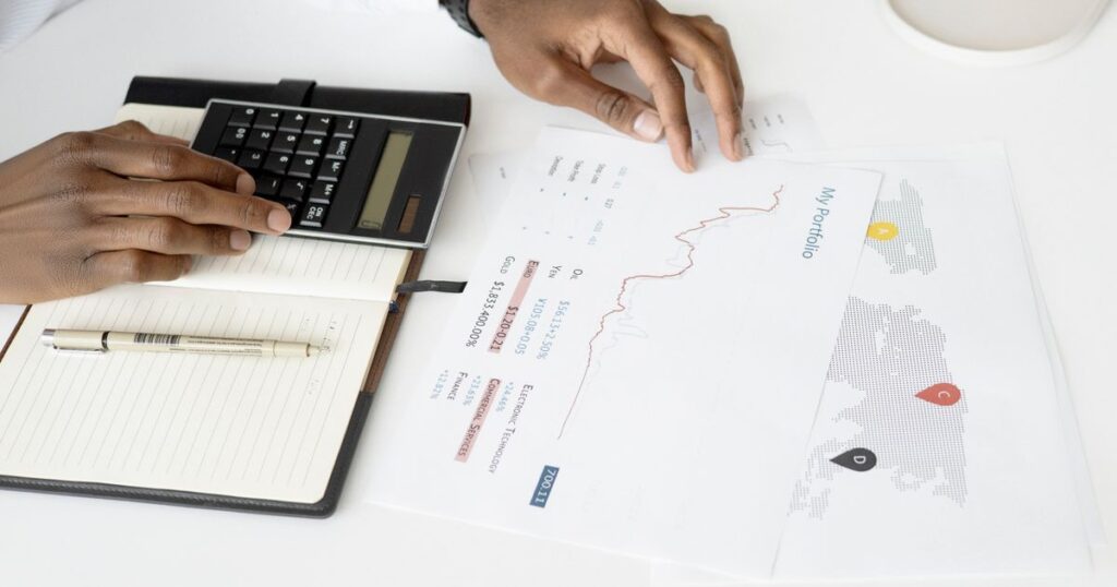 Overhead view of a person using a calculator to work through profit figures on financial documents.