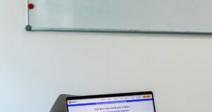 Modern office desk with a laptop beside a whiteboard holding a weekly social media posting schedule.