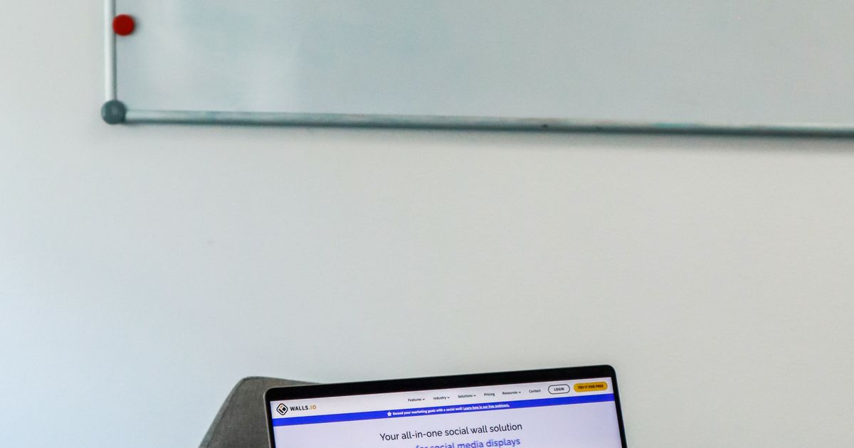 Modern office desk with a laptop beside a whiteboard holding a weekly social media posting schedule.