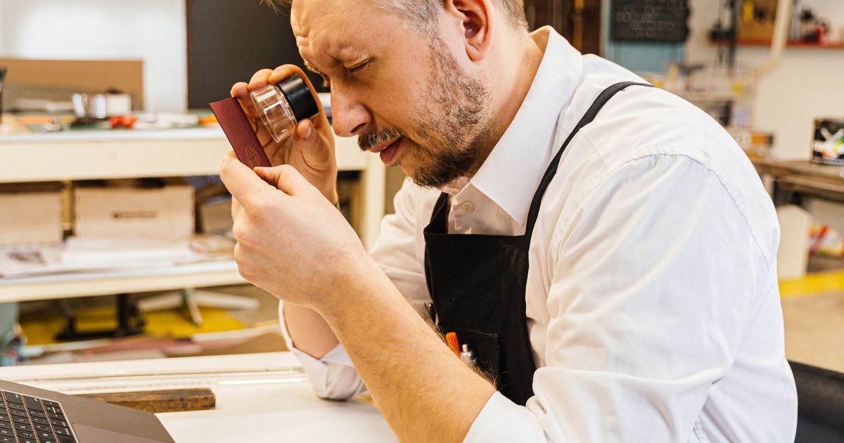 Marketer using a magnifying glass to examine printed detail closely at a studio workbench.