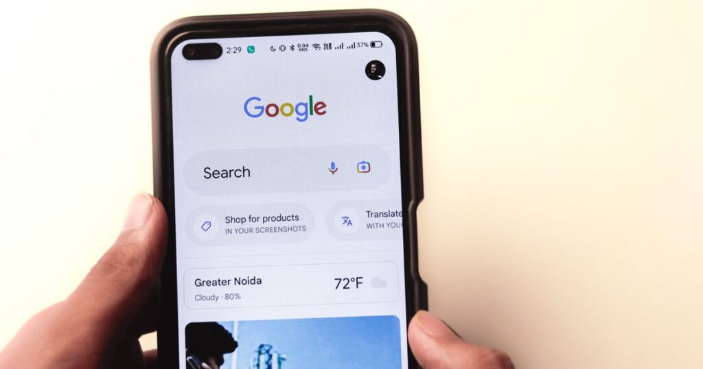 Hand holding a smartphone with the Google search app open, where AI Overviews now appear above the results