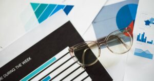 Reading glasses resting on printed reports full of bar charts and graphs