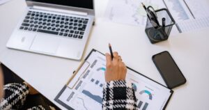 Marketer reviewing a printed dashboard of conversion rate and new customer charts beside a laptop and phone