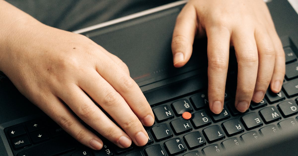 Close-up of hands typing on a laptop keyboard while drafting SEO prompts