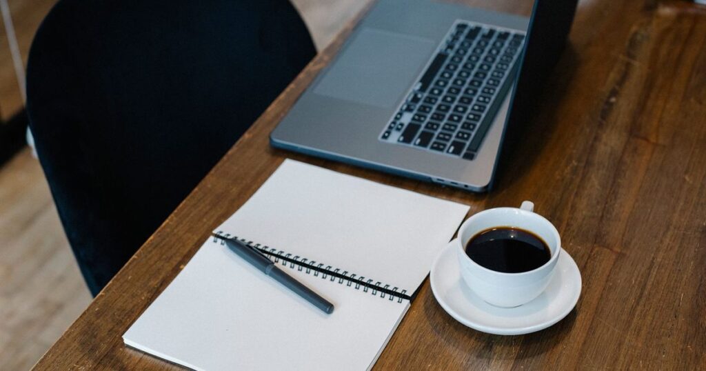 Laptop, notebook and a cup of coffee on a wooden desk in a quiet workspace