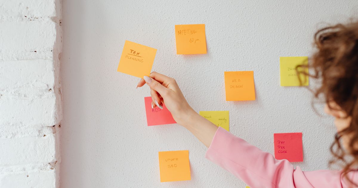 A marketer arranging coloured sticky notes of marketing tasks across a white wall while planning a schedule