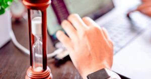 An hourglass running beside a laptop and a hand reaching for the keyboard, illustrating the wait for a slow-loading web page