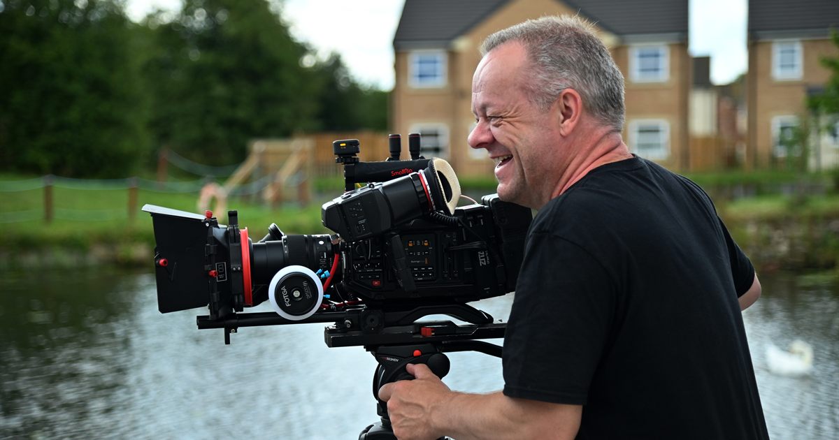 A camera operator filming on location with a rigged cinema camera on a fluid-head tripod, the crew and equipment that make up most of a video production quote.