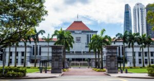 Singapore Parliament House seen from the road, framed by palm trees with the city skyline behind