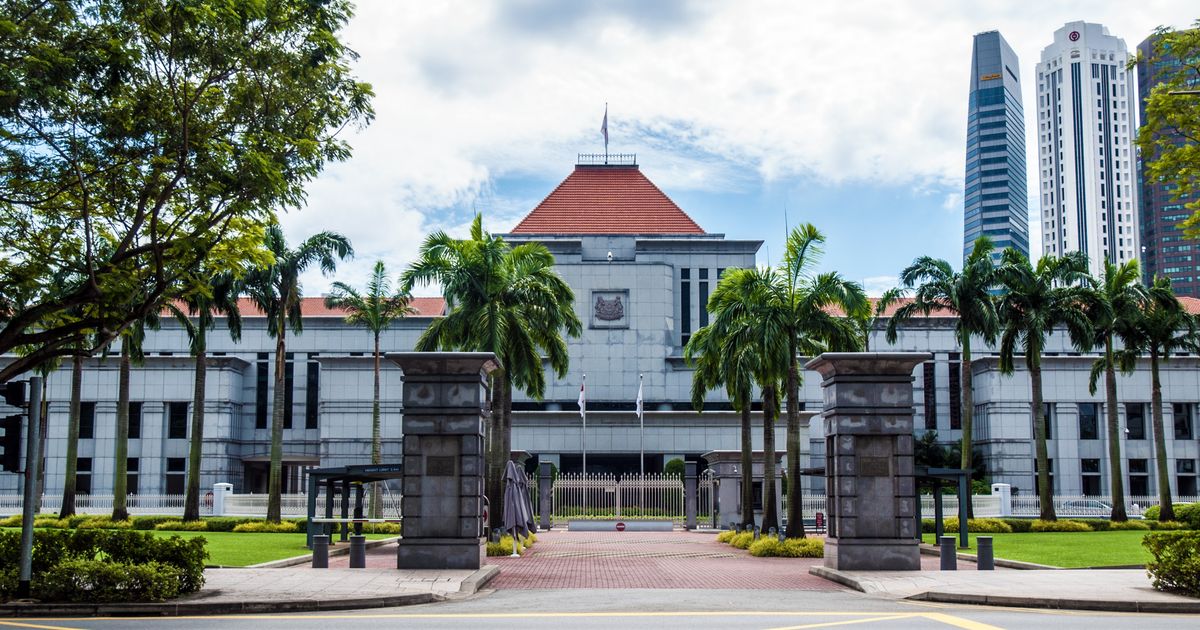 Singapore Parliament House seen from the road, framed by palm trees with the city skyline behind