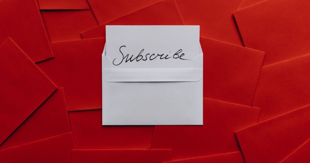 A white envelope holding a handwritten Subscribe card, lying on a spread of red envelopes