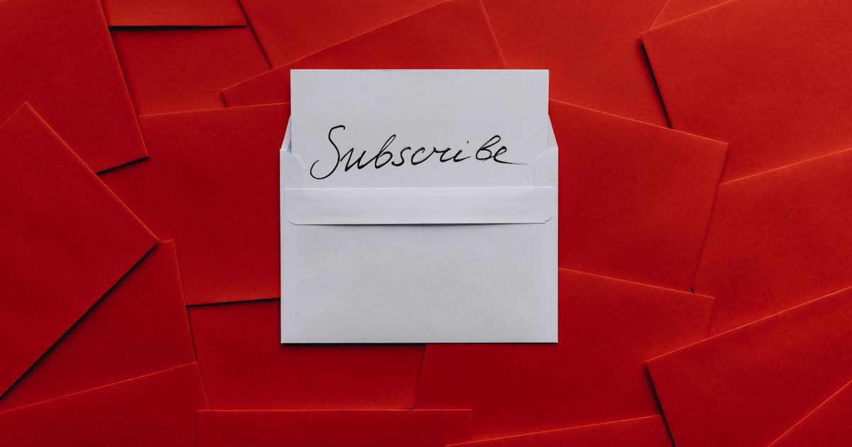 A white envelope holding a handwritten Subscribe card, lying on a spread of red envelopes