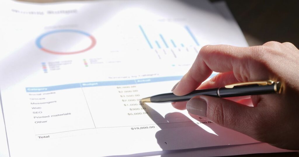 A hand holding a pen over a printed marketing budget showing an SEO line item and a total