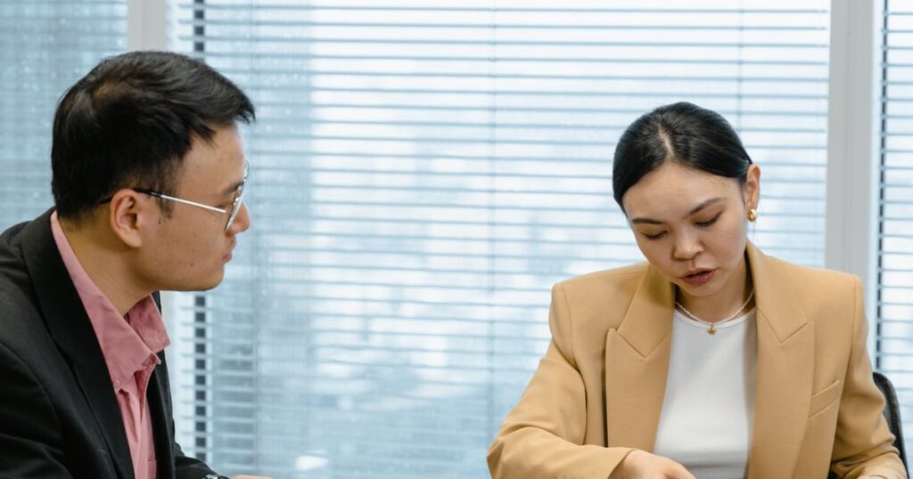 Two professionals reviewing documents together across a table in a bright office meeting room