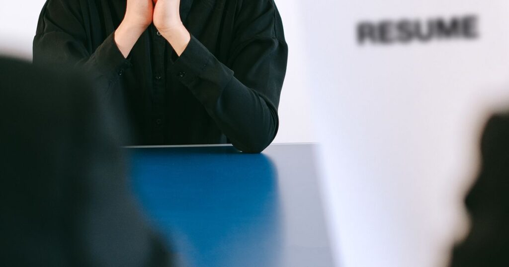 A job candidate seated at an interview table beside a document marked Resume