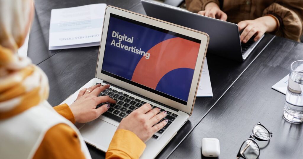 Two marketers working on laptops with a digital advertising campaign open on screen in an office