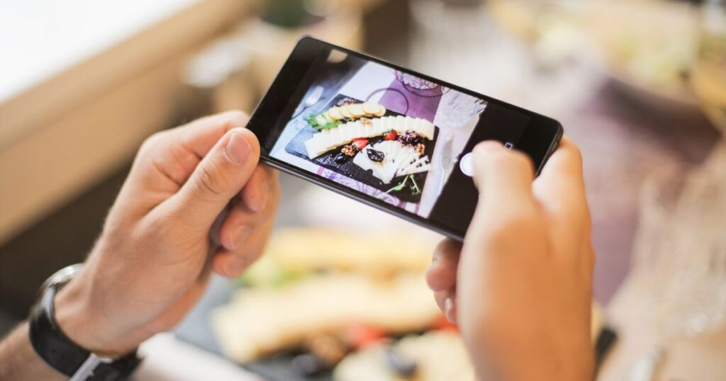 Diner photographing a plated dish on a smartphone at a restaurant table