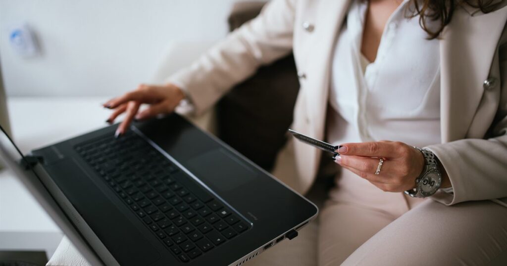 Business owner holding a credit card while paying on a laptop at a home workspace