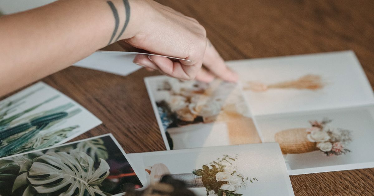 A hand selecting from printed photographs spread across a wooden table while choosing which images to use