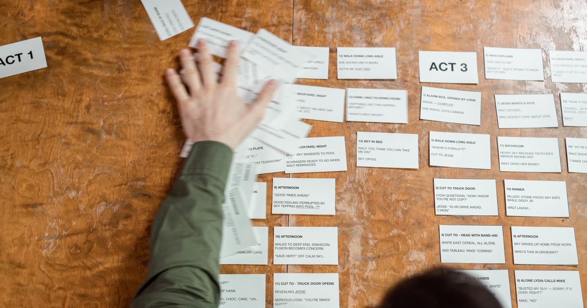 A person laying out numbered scene cards and act headings across a wooden table while planning a video script