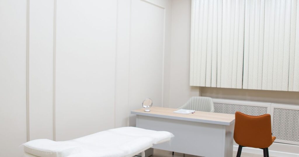 Bright, empty clinic consultation room with an examination couch, desk and chairs