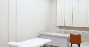 Bright, empty clinic consultation room with an examination couch, desk and chairs