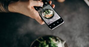 Diner photographing a plated Asian dish on a smartphone at a restaurant table