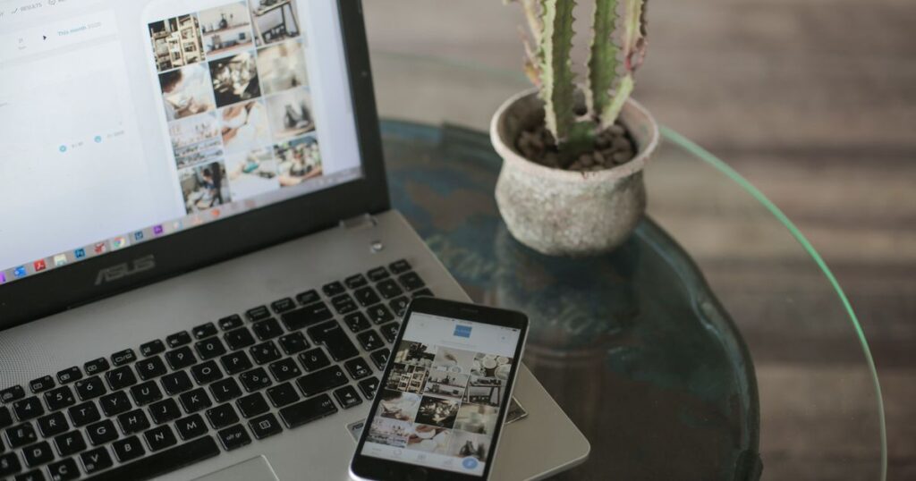 A laptop and smartphone side by side on a desk showing a grid of social media content
