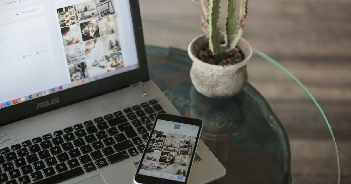 A laptop and smartphone side by side on a desk showing a grid of social media content