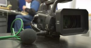 A professional video camera and a foam-shielded microphone set up on a table ready for an interview