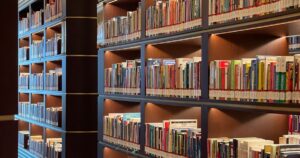 Rows of neatly organised library shelves filled with books in a lit reading room