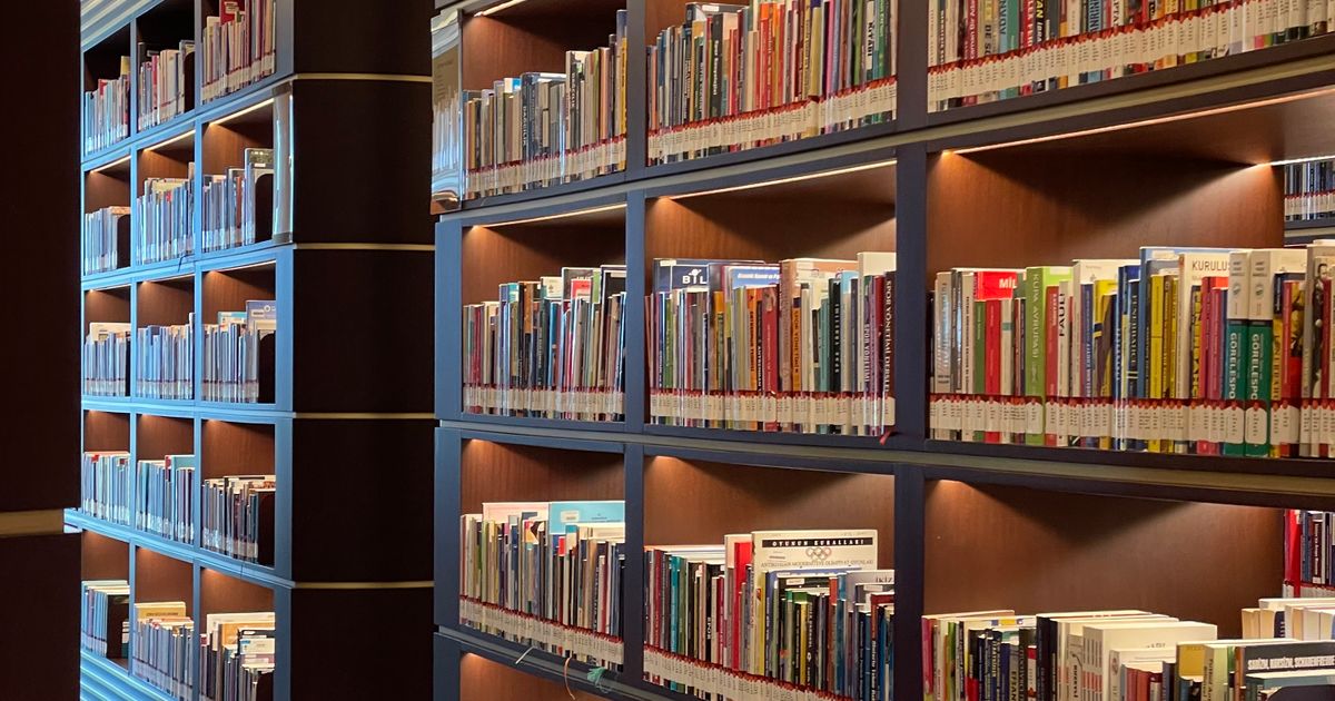 Rows of neatly organised library shelves filled with books in a lit reading room