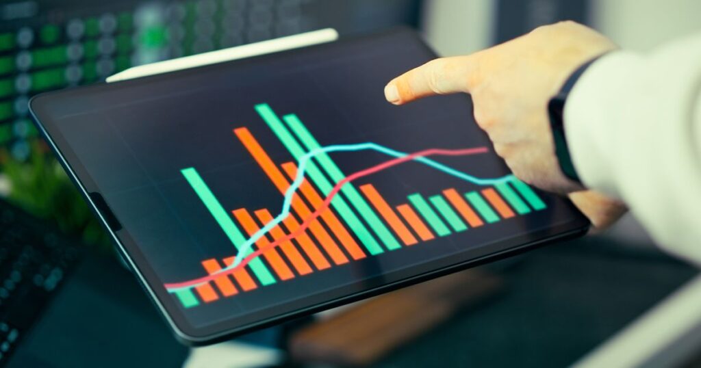 Hand pointing at a tablet screen showing bar and line charts of traffic performance data