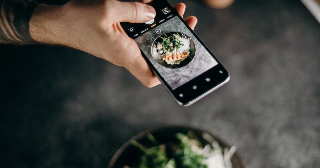 A diner photographing a plated dish with a smartphone camera at a restaurant table
