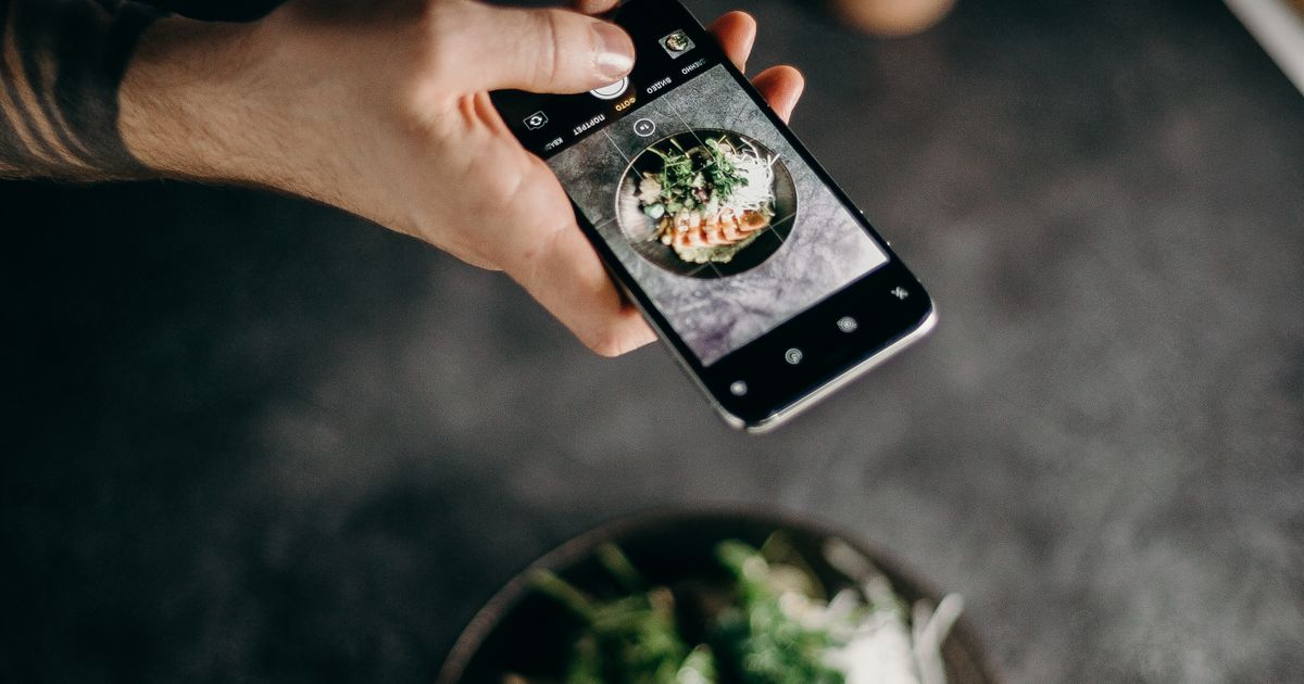 A diner photographing a plated dish with a smartphone camera at a restaurant table